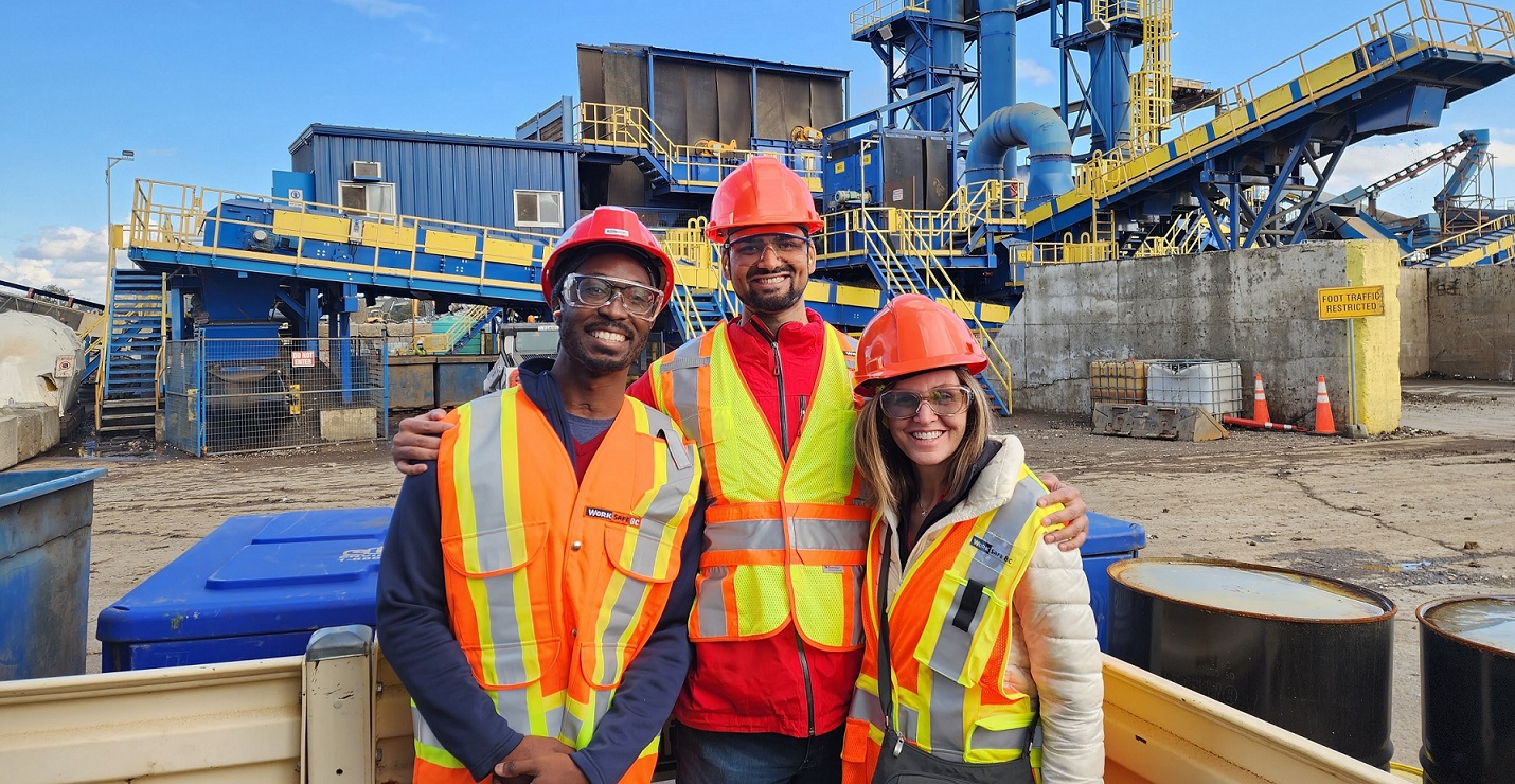 Three people standing in front of the steel shredder at Richmond Steel Recycling in Vancouver
